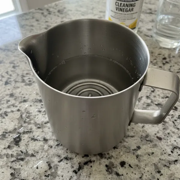 Automatic milk frother filled with a white vinegar and water solution for descaling mineral deposits.