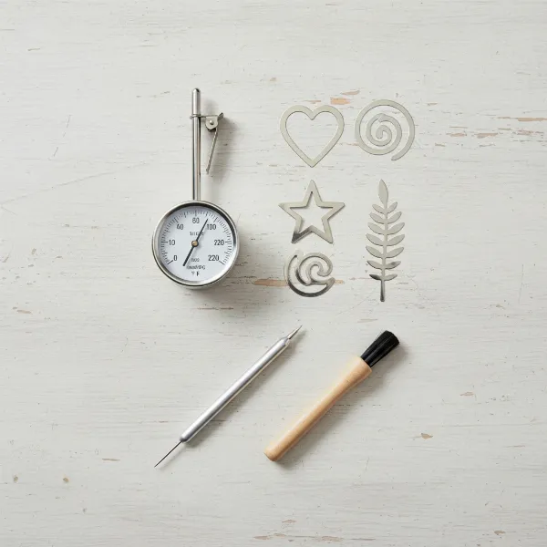 An assortment of home barista tools including a thermometer, latte art stencils, and an etching pen.
