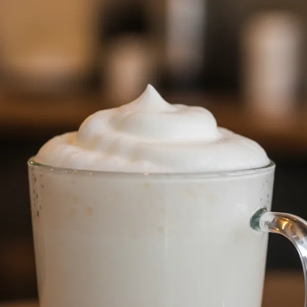 Close-up of perfectly frothed milk in a glass mug, rich and dense texture.